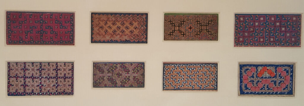 Four different designs of rugs hanging on a wall.